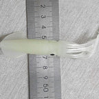 Clear plastic tube with a white string-like material, measured against a ruler on a textured gray background.