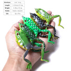 Hand holding a set of 5 lifelike soft frog fishing lures with double hooks, measuring 2.16 inches (5.5 cm) and weighing 0.55oz (15.6g), assorted colors for bass and pike fishing.